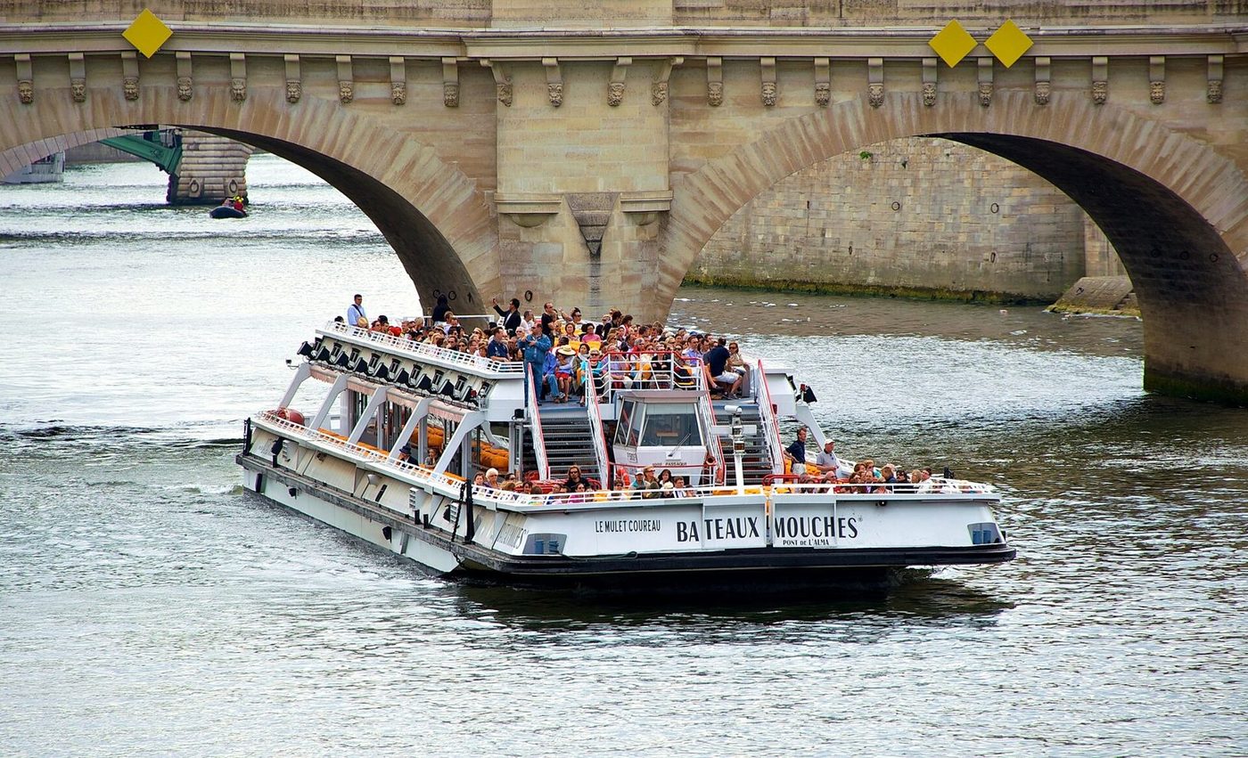 Un bateau-mouche chargé de passagers passe sous un pont de Paris